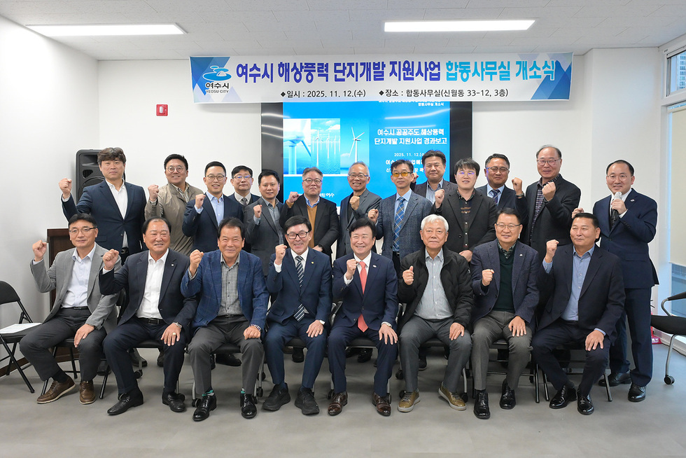 ‘여수시 해상풍력 단지개발 지원사업 합동사무실 개소식 일시: 2025년 11월 12일 (수) /  장소:합동사무실(신월동 33-12,3층)’이라고 적힌 현수막 앞에서 정기명 여수시장과 관계자들이 단체로 서서 주먹을 들어 올리며 기념촬영하는 모습.