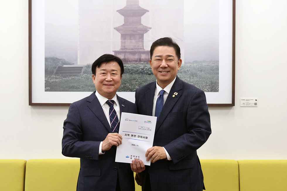 정기명 여수시장이 국회를 방문해 국비 증액을 요청하는 현안 건의 문서를 국회의원에게 전달하는 모습. 두 사람은 문서를 함께 들고 기념촬영을 하고 있으며, 문서 표지에는 ‘지역 현안 건의사업’이라는 문구가 적혀 있다. 뒤편에는 불탑 사진이 걸린 액자가 보인다.