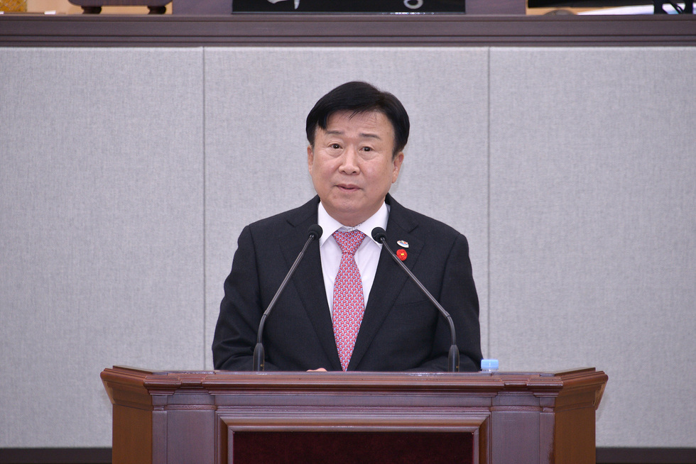 정기명 여수시장이 본회의장 연단에서 마이크 두 개 앞에 서서 시정연설을 하고 있는 모습. 정장은 검은색 재킷과 빨간 넥타이를 착용하고 있다