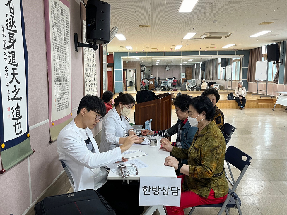 의사와 환자들이 상담을 진행하는 장면으로, 한방 상담 부스에서 여러 명의 노인이 상담을 받고 있다.
