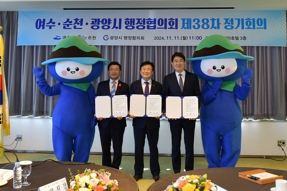 여수, 순천, 광양시의 행정협의회 제38차 정기회의에서 관계자들이 서명한 모습과 함께 두 개의 캐릭터가 참석하고 있다.