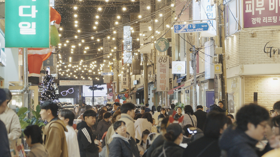 사람들이 붐비는 거리에서 다양한 상점과 조명이 있는 모습으로, 거리에는 노래방과 피부 관리 관련 간판이 보인다.