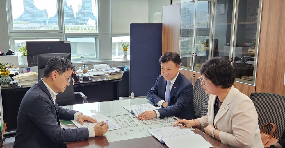 정기명 여수시장이 국회 사무실에서 두 명의 관계자와 함께 책상 위 문서를 검토하며 협의하는 모습. 창밖으로 빌딩 전경이 보인다