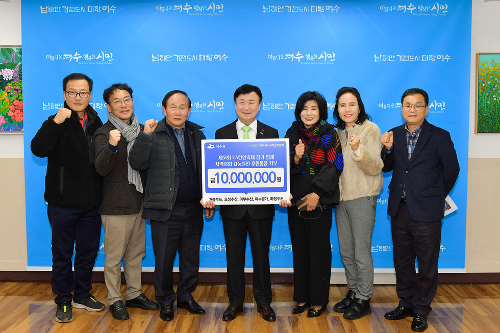 여섯 명의 사람들이 기부금 전달식에서 포즈를 취하고 있으며, 중앙에 있는 남성이 기부금을 들고 있다. 배경에는 기부와 관련된 문구가 적힌 파란색 현수막이 있다.