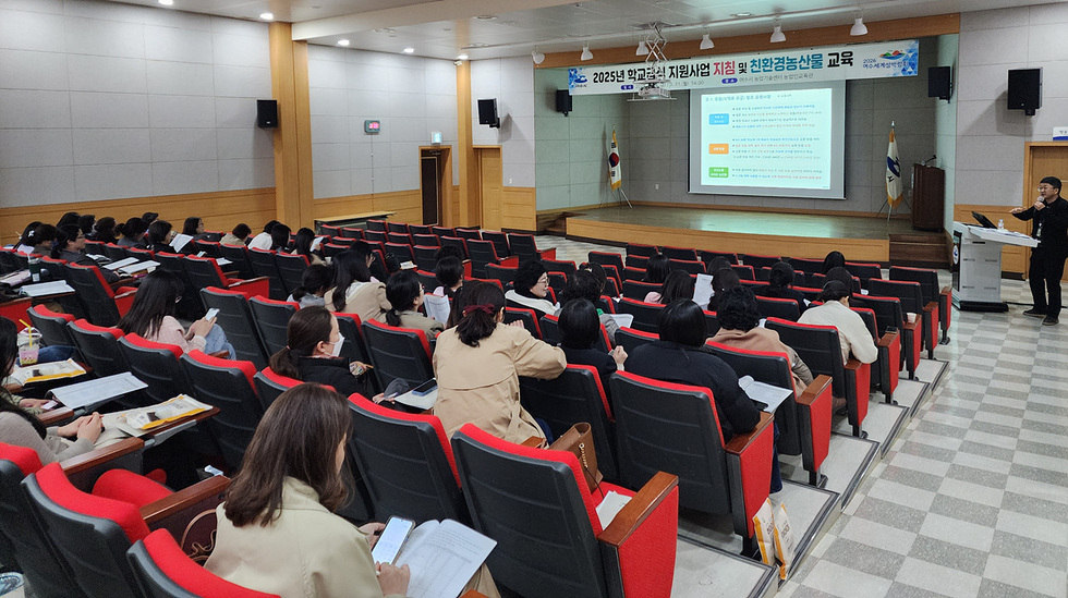강의실에서 교육을 받는 참석자들이 있으며, 강사가 화면을 통해 친환경농산물 교육 내용을 설명하고 있다.