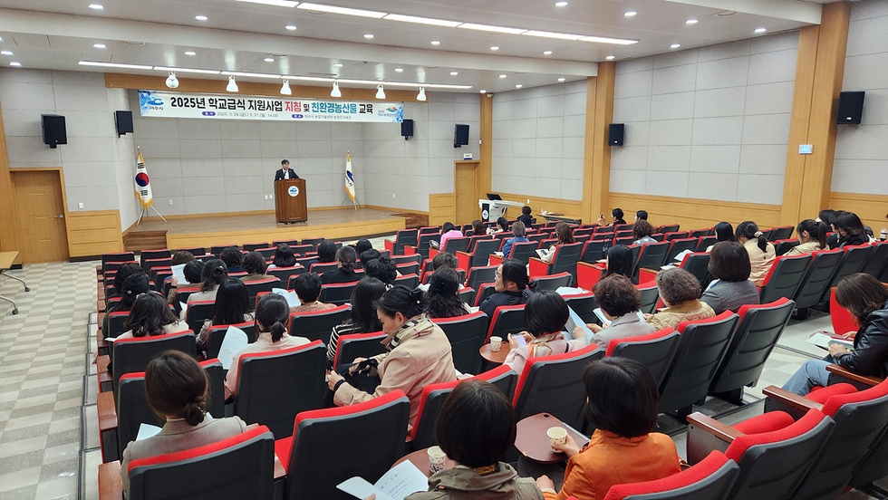 2025년 학교급식 지원사업 지침 및 친환경농산물 교육을 주제로 한 행사에서 발표자가 연단에 서 있고, 청중이 강의를 듣고 있는 모습