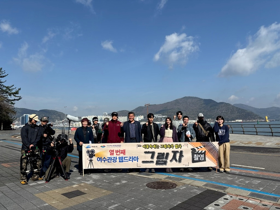 여수에서 열 번째 여수관광 웰드라마 촬영을 위해 모인 배우와 스태프들이 현수막 앞에서 포즈를 취하고 있다.