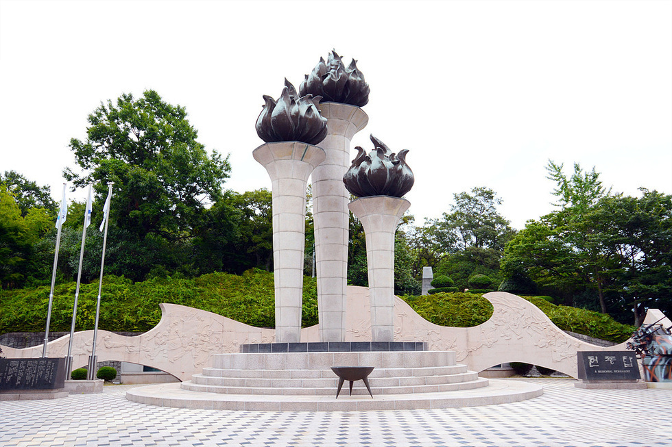 세 개의 불꽃 모양 조각상이 있는 기념비가 있는 공원 풍경으로, 주변에는 나무와 조경이 잘 되어 있다.