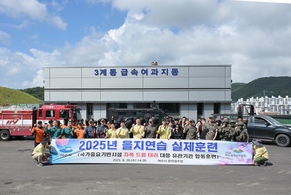여수시에서 2025년 을지연습 실전훈련을 위해 여러 기관 관계자들이 모여 단체 사진을 찍고 있다. 배경에는 3계통 급속여과 지동 건물이 보인다.