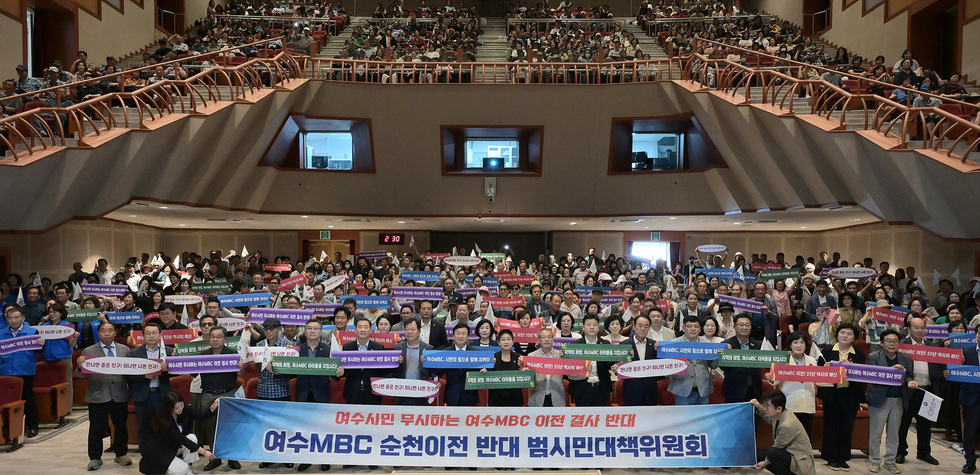 여수MBC의 순천 이전에 반대하는 시민들이 모여 현수막을 들고 있는 모습으로, 많은 사람들이 참석한 행사장 내부가 보인다.