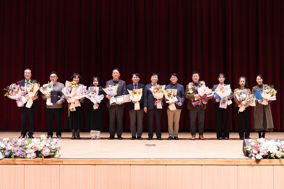 여수문화홀 무대 앞에서 2025년 자랑스러운 여수 기업인 시상식을 마친 수상자와 관계자들이 꽃다발과 상패를 들고 나란히 서서 기념촬영을 하고 있는 모습