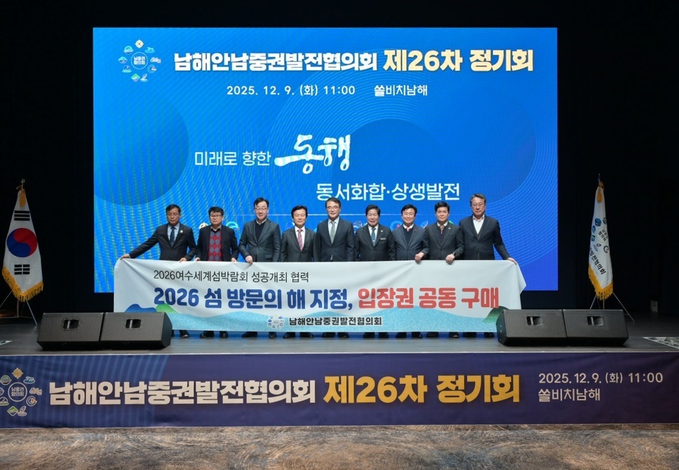 무대 중앙 대형 스크린 앞에서 남해안남중권발전협의회 관계자들이 줄지어 서서 ‘2026여수세계섬박람회 성공개최 협력 – 2026 섬 방문의 해 지정, 입장권 공동 구매’ 문구가 적힌 현수막을 펼쳐 들고 기념촬영을 하고 있다. 상단에는 ‘남해안남중권발전협의회 제26차 정기회’, ‘2025.12.9.(화) 11:00 쏠비치남해’ 문구가 표시되어 있다.