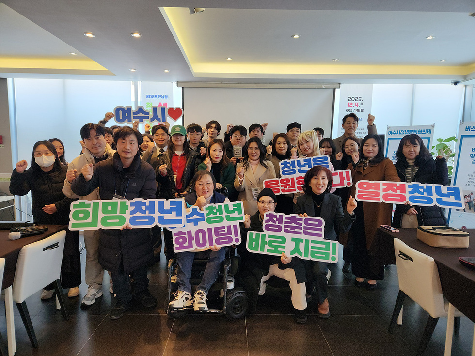 2025년 청년공동체 활성화사업 성과공유회 행사장에서 여러 청년 참가자들이 단체로 서서 주먹을 쥐고 포즈를 취하고 있다. 전면에는 ‘희망청년’,‘여수청년 화이팅!’ ,‘청년을 응원합니다!’, ‘열정청년’, ‘청춘은 바로 지금!’ 등의 문구가 적힌 손피켓을 든 참가자들이 자리하고 있다. 